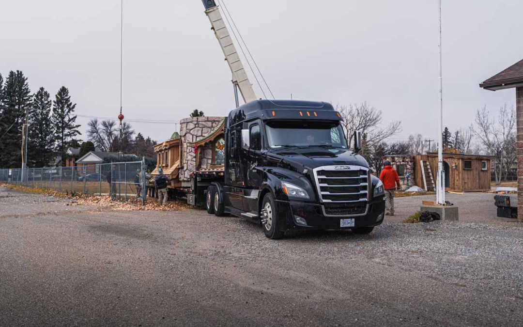 Evans Trucking black semi with RGN trailer delivering a playhouse at a construction site with a crane and workers.
