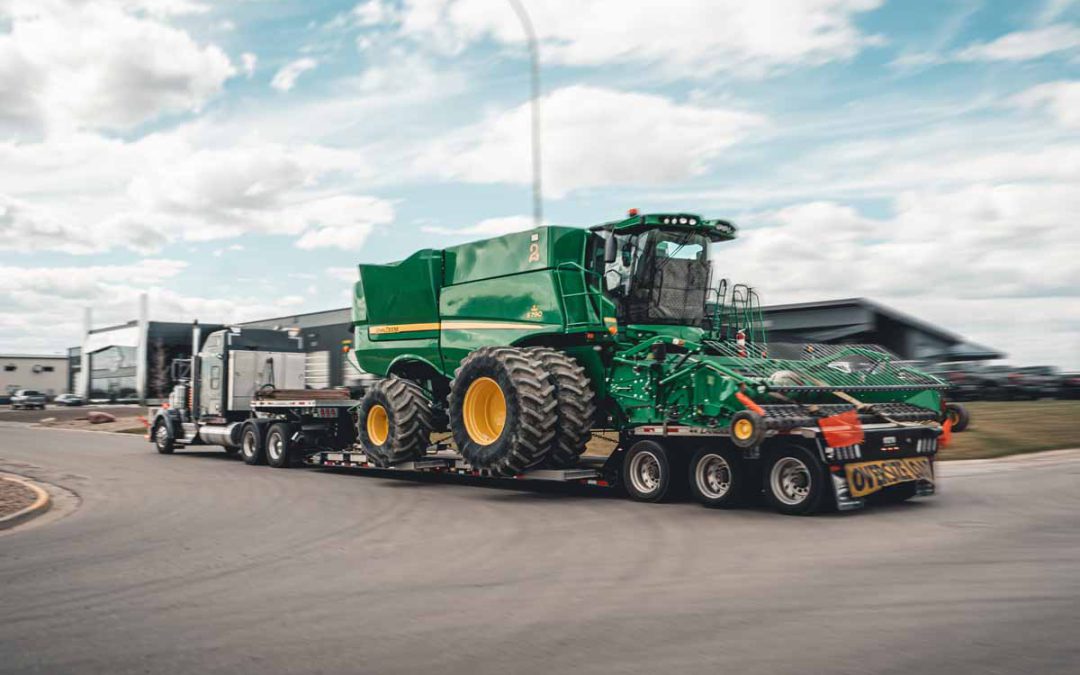 Evans Trucking RGN hauling oversized John Deere combine with oversize load signage.