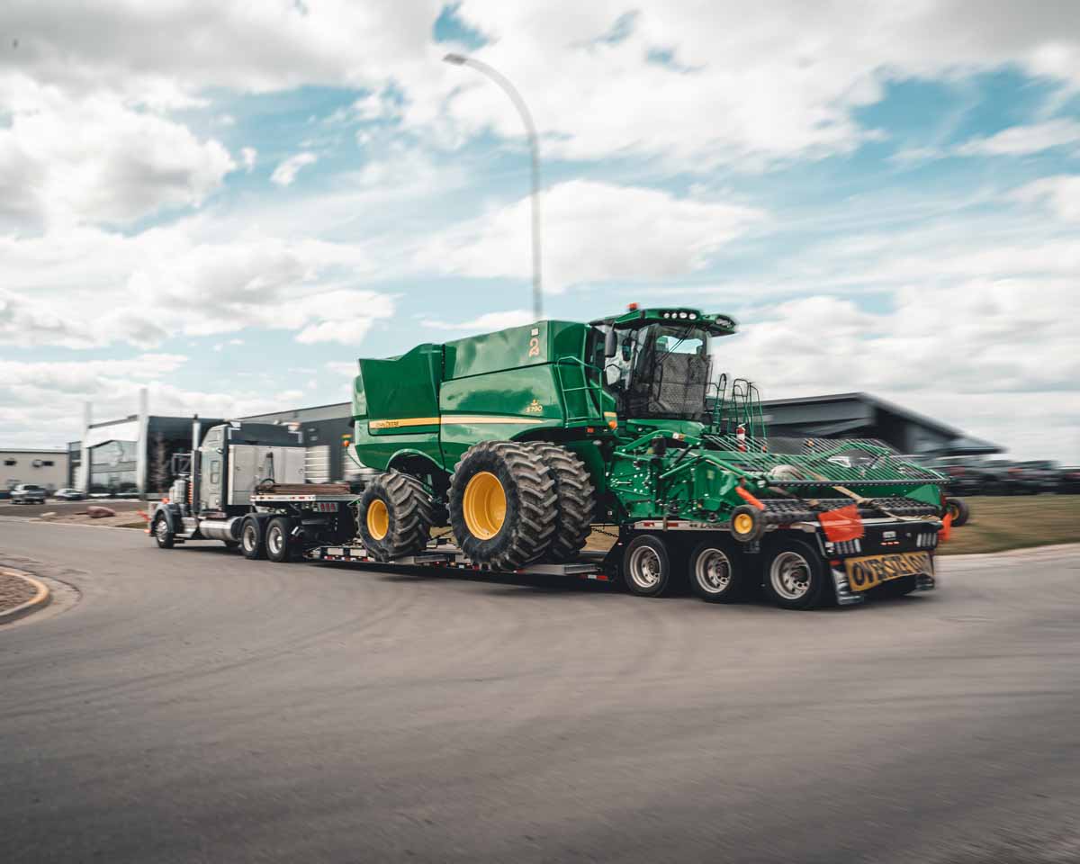 Evans Trucking RGN hauling oversized John Deere combine with oversize load signage.